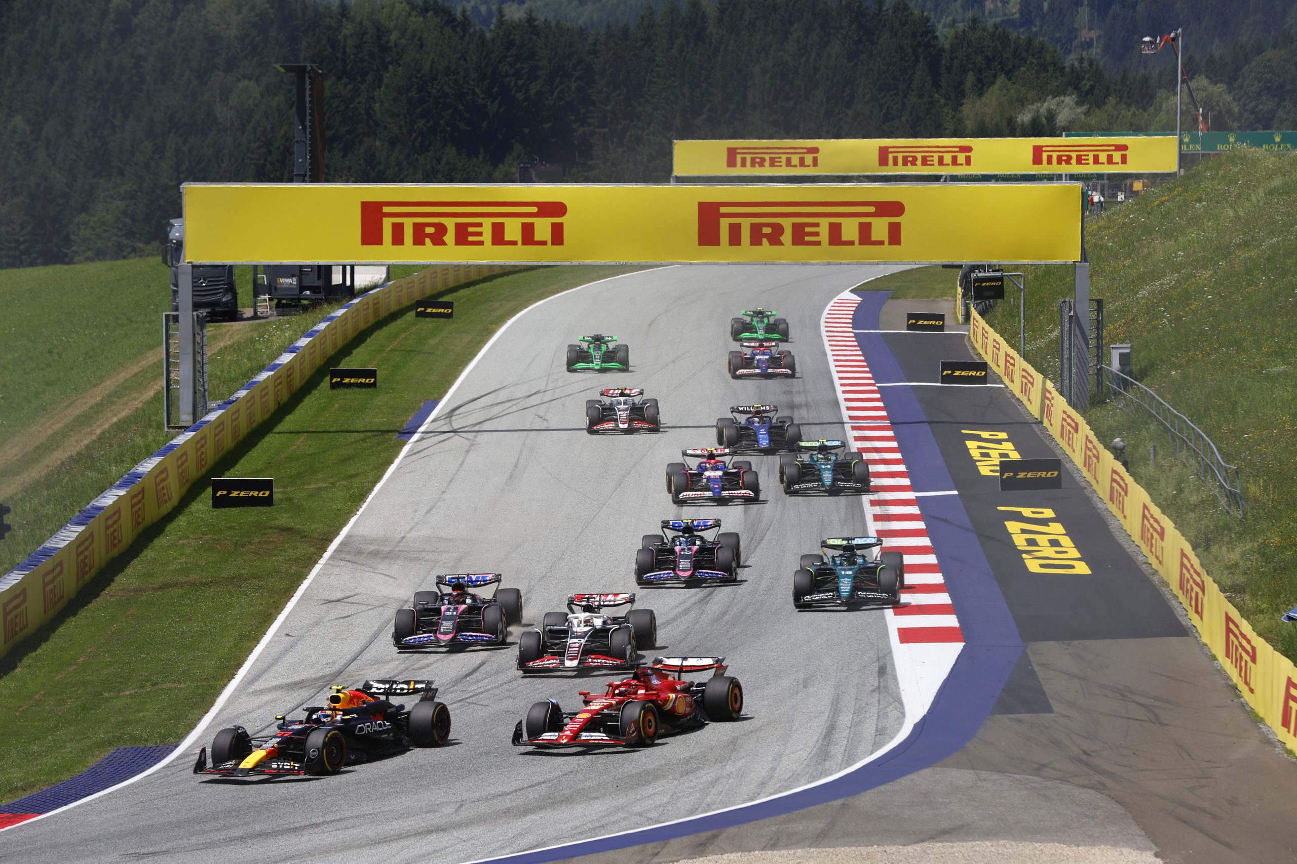Red Bull Racing Formula 1 car driving at the Red Bull Ring during the Austria Grand Prix with blurred yellow wildflowers in the foreground and Styrian mountains in the background.