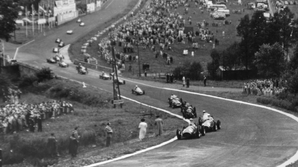 Vintage open‑wheel race cars navigating a bend on the historic Spa‑Francorchamps road circuit with spectators lining the roadside.