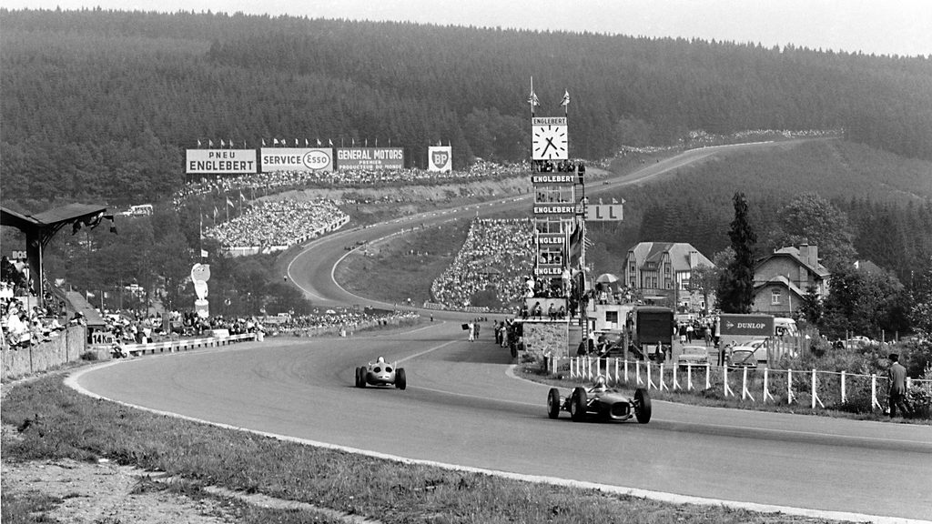 Historic Formula One cars racing at Spa‑Francorchamps with Englebert timing tower and large spectator crowds.