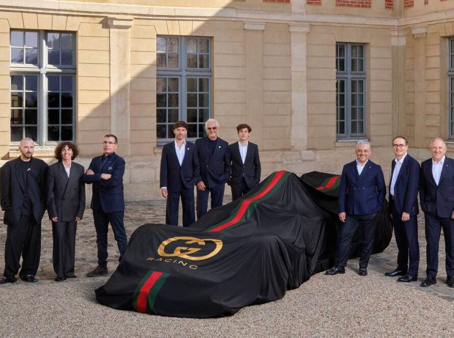 Executives and representatives from Alpine and Gucci stand beside a covered race car featuring Gucci’s signature colors, marking the announcement of a new partnership between the two brands.