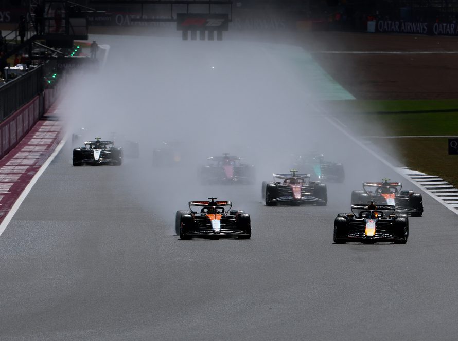 Formula 1 cars racing through heavy spray in wet conditions at Silverstone.