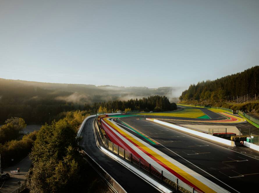 Raidillon at Spa‑Francorchamps in morning mist with forested hills and painted runoff areas.